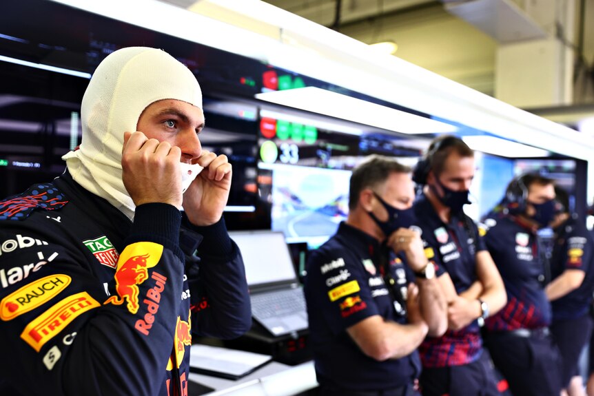 Max Verstappen puts his face guard on while standing with Red Bull team members