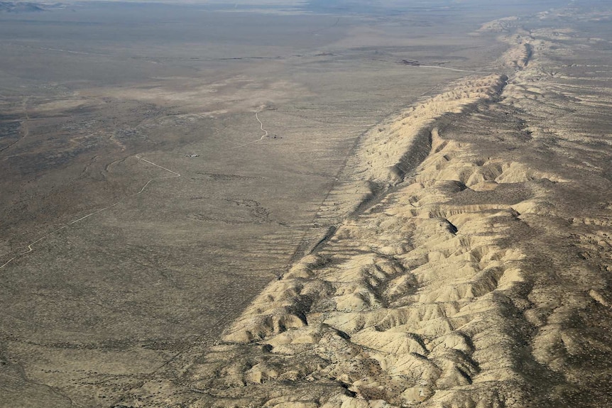 An aerial photo shows a desert plain with a marked line of hills and streams marking its right side.