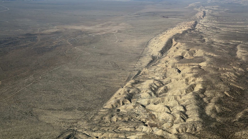 An aerial photo shows a desert plain with a marked line of hills and streams marking its right side.