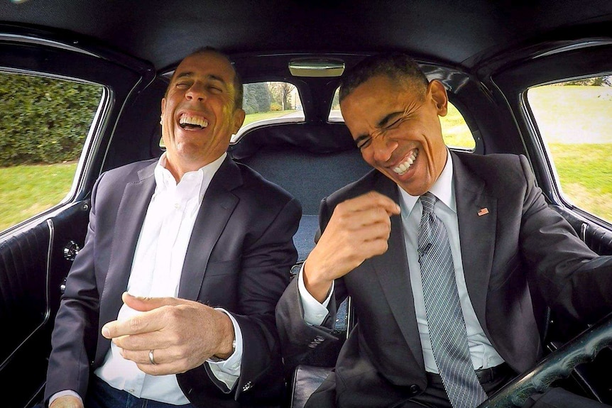 Barack Obama laughs while driving a 1963 Corvette with Jerry Seinfeld in the passenger seat.