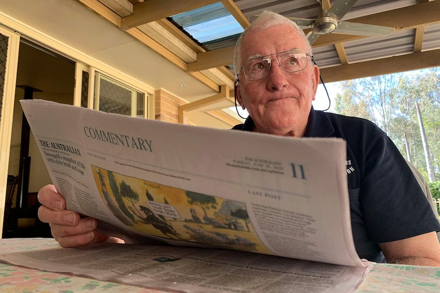 A man staring grim-faced over the top of his newspaper while sitting in his backyard