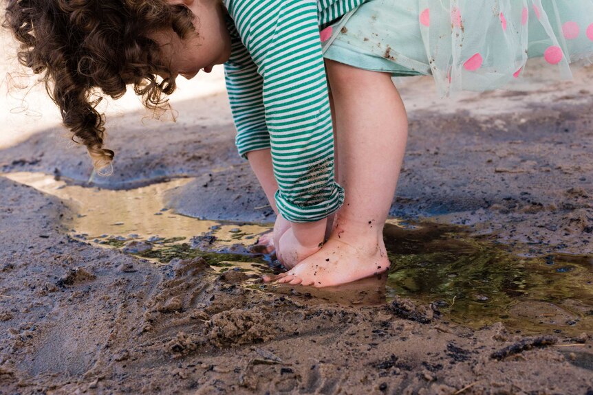 A little girl bends over to play with sand and water.