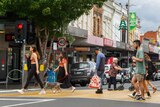 Pedestrians walk across a crossing on a Moonee Ponds street, with Christmas decorations hanging from shops.