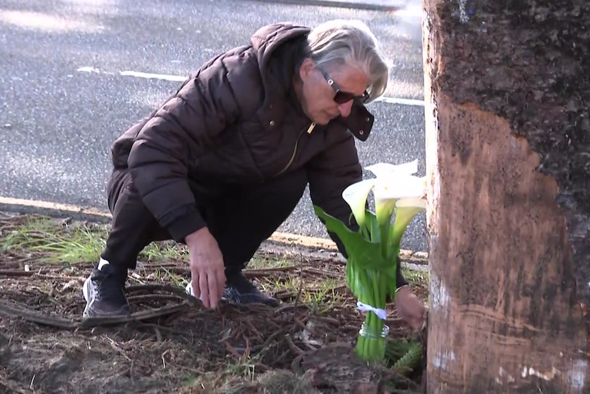 A man lays flowers next to a tree