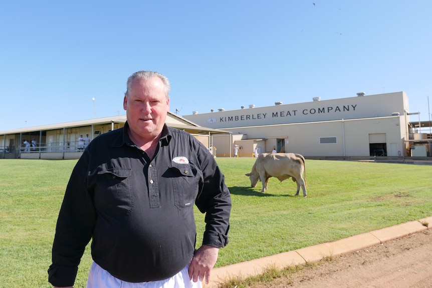 a man in a black top stands in front of a factory