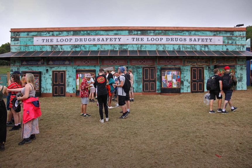 Young men and women stand on the grass outside a large green tent.