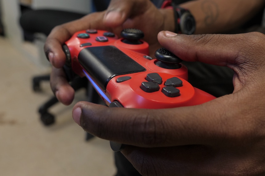 An close up a hands holding a red Playstation 4 controller.