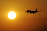 A plane flies towards a setting sun.