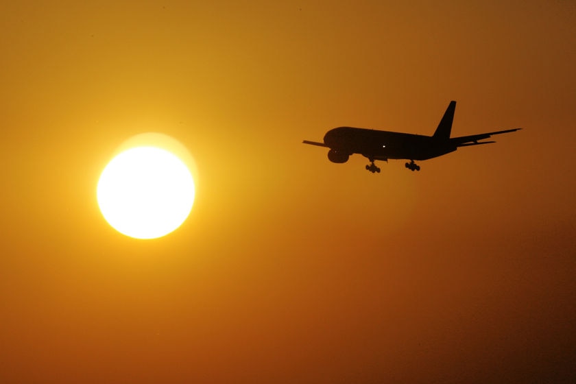 A plane flying into the sun as it is setting.