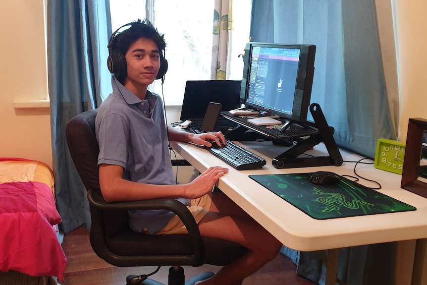 A teenage boy sits at his computer in his room, wearing headphones.