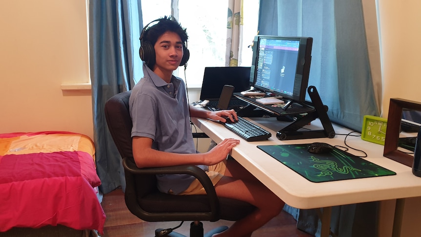 A teenager sits in his room, working on a computer.
