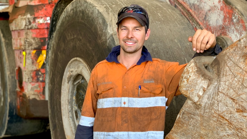 A man in a high vis shirt standing next large mining machinery.