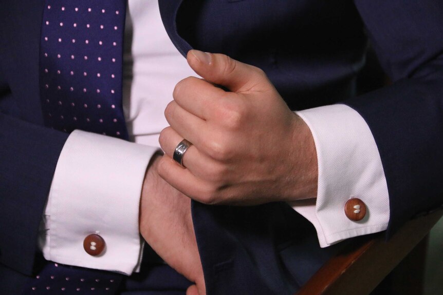 Tim Wilson adjusting his cufflinks with his engagement ring on full display.