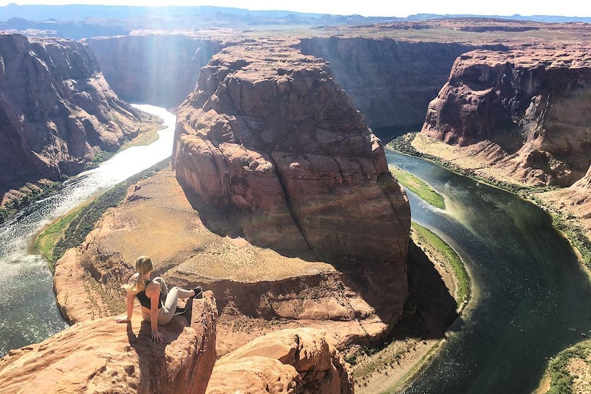 A woman sits near the edge of the overlook of Horseshoe Bend.
