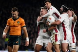 A group of England players celebrate scoring a try as a Wallabies player walks past.