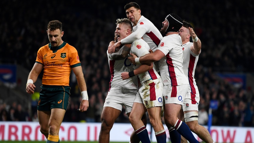 A group of England players celebrate scoring a try as a Wallabies player walks past.