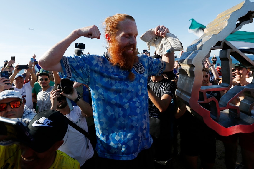 A red haired man cheering surrounded by a crowd. 