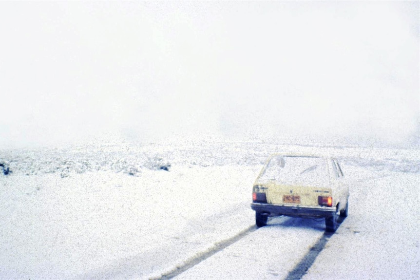 An 80s car on a track surrounded by snow.