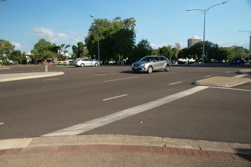The intersection of two Darwin streets, with a silver car in foreground and a white one travelling in opposite direction