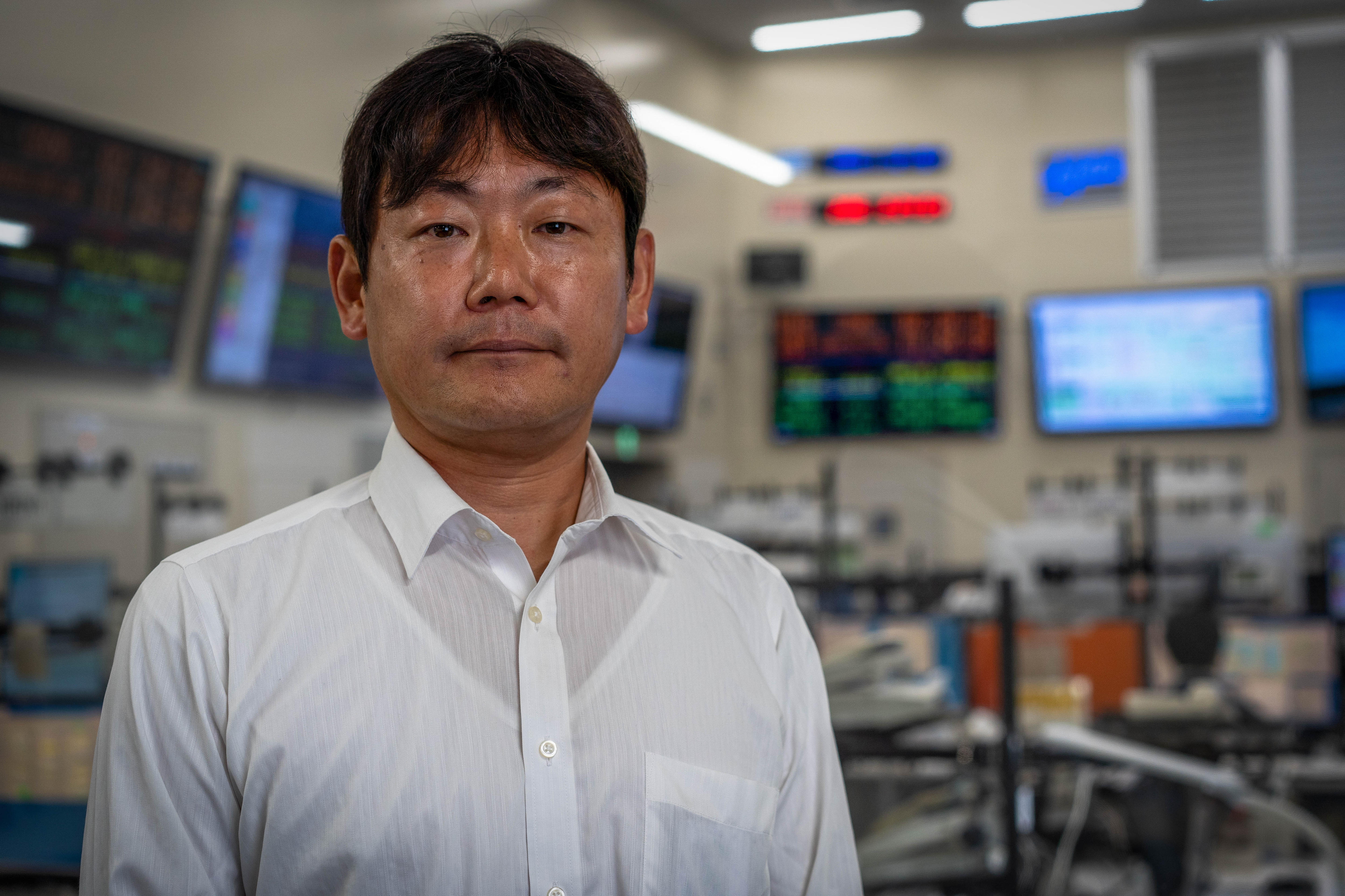 A Japanese man stands in front of a lot of computers