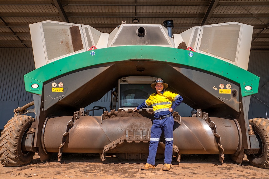 a man stands in front of a strange looking large farm machine.