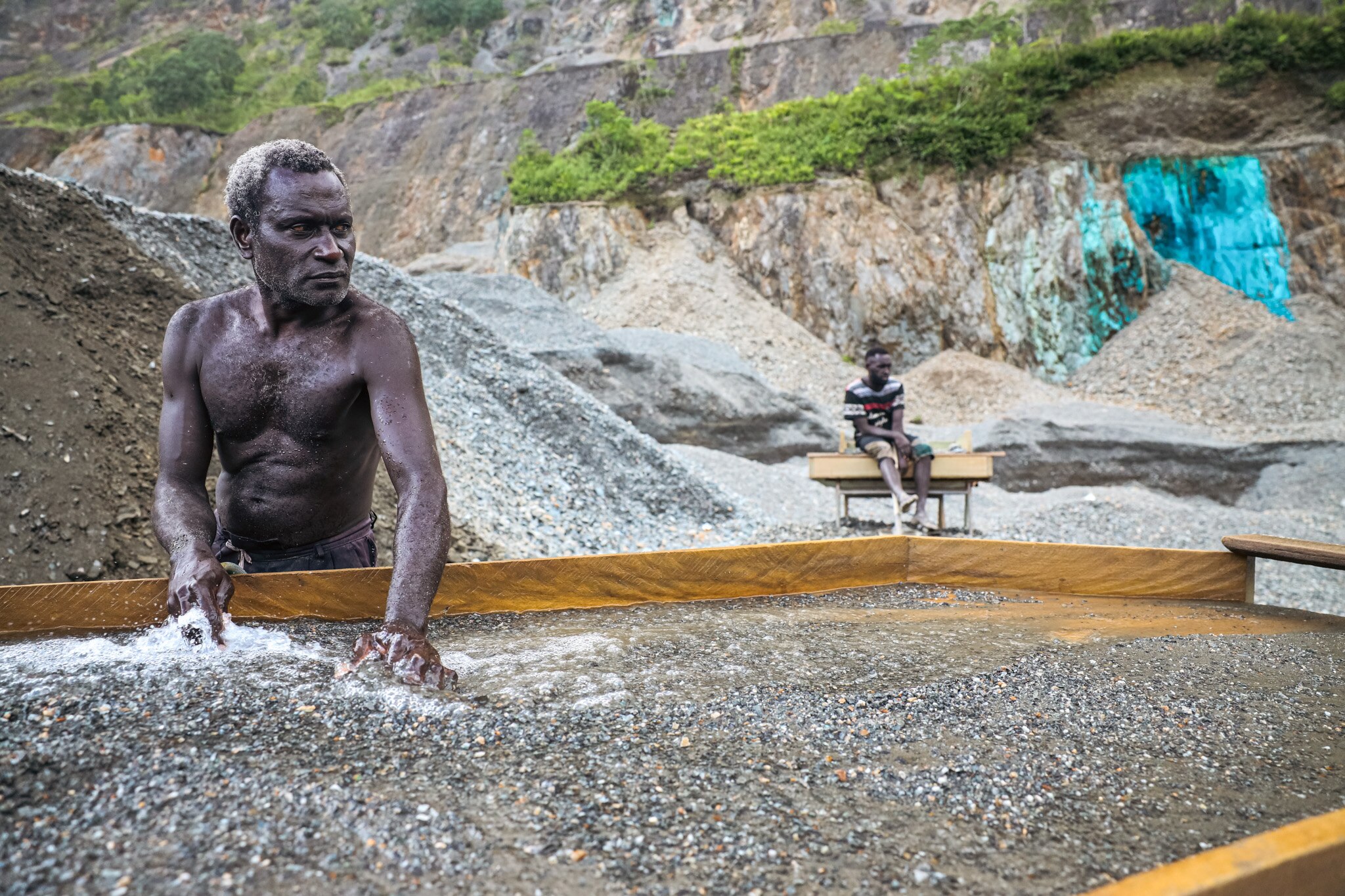A man pans for gold while another man looks on.