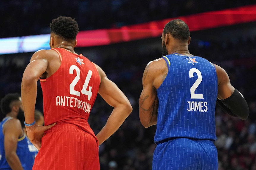 Two male basketball players stand next to each other with their backs turned at the NBA All-Star Game.