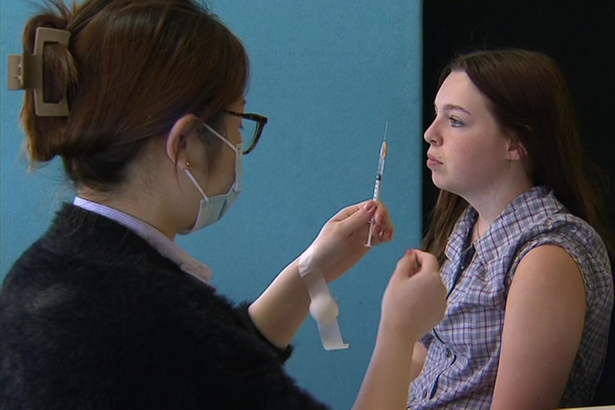 A woman gets a needle ready to vaccinate a young woman in school uniform