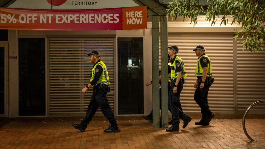A group of police officers walk down a street in front of a shop front at night 