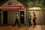 A group of police officers walk down a street in front of a shop front at night 