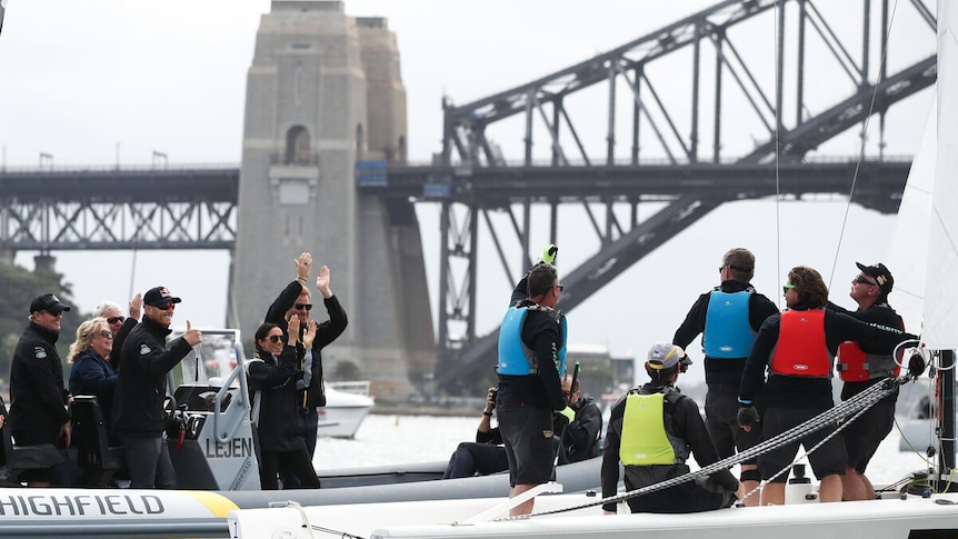 Men stand on a yacht near the Sydney Harbour Bridge, as Prince Harry and Meghan cheer them on from another boat.