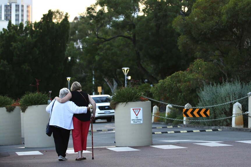 Two women embrace as they walk away from the camera towards a garden
