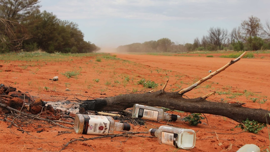Empty bottles of spirits on a red dirt road.