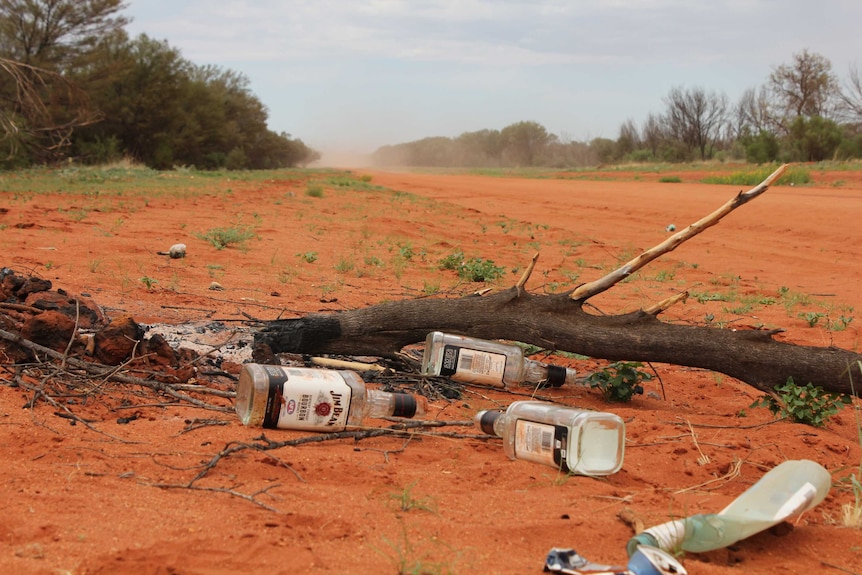 Empty bottles of spirits on a red dirt road.