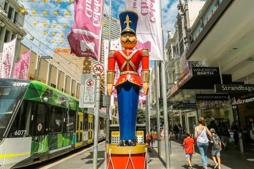 A giant figure of the little drummer boys stands tall over a tram and shoppers in Melbourne's Bourke Street.