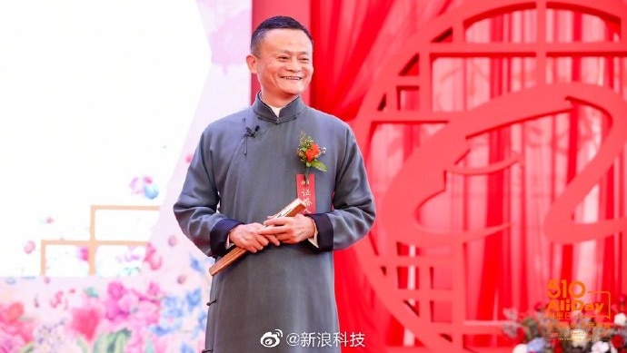 Jack Ma smiles on stage in front of a red background as he addresses his employees.