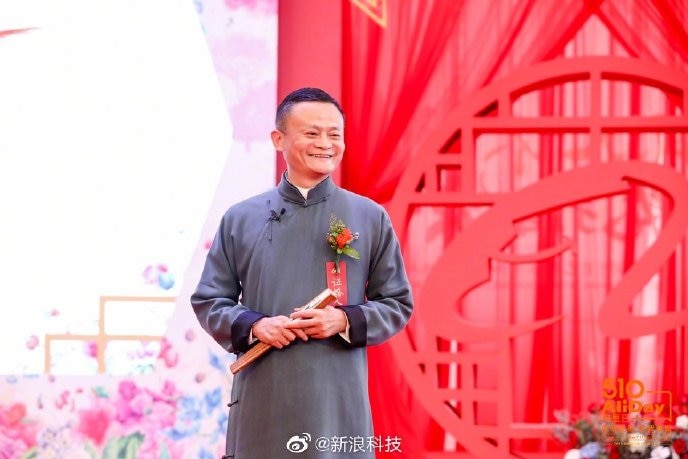 Jack Ma smiles on stage in front of a red background as he addresses his employees.