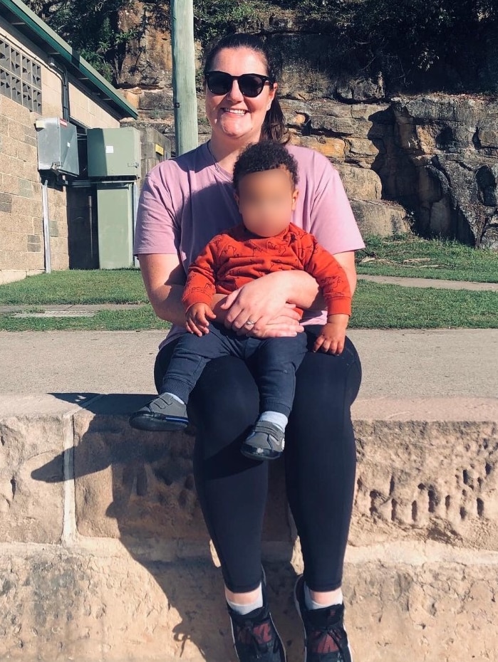 A woman sits on a cement wall, holding a baby on her lap