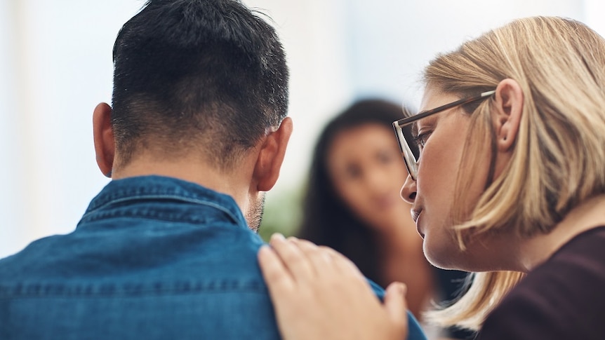 A woman puts her hand on a mans should, offering comfort.