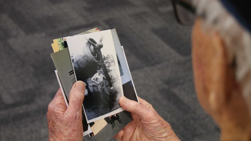 An old man holds and looks at a photo of his younger self with a bomber plane.
