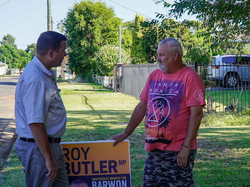 two men stand facing each other talking outside a house