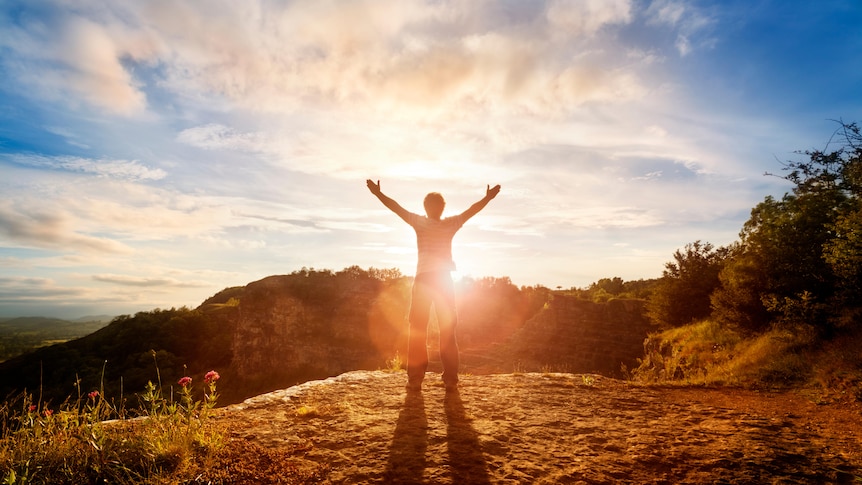 man's silhouette with arms stretched out wide and sun's rays in nature