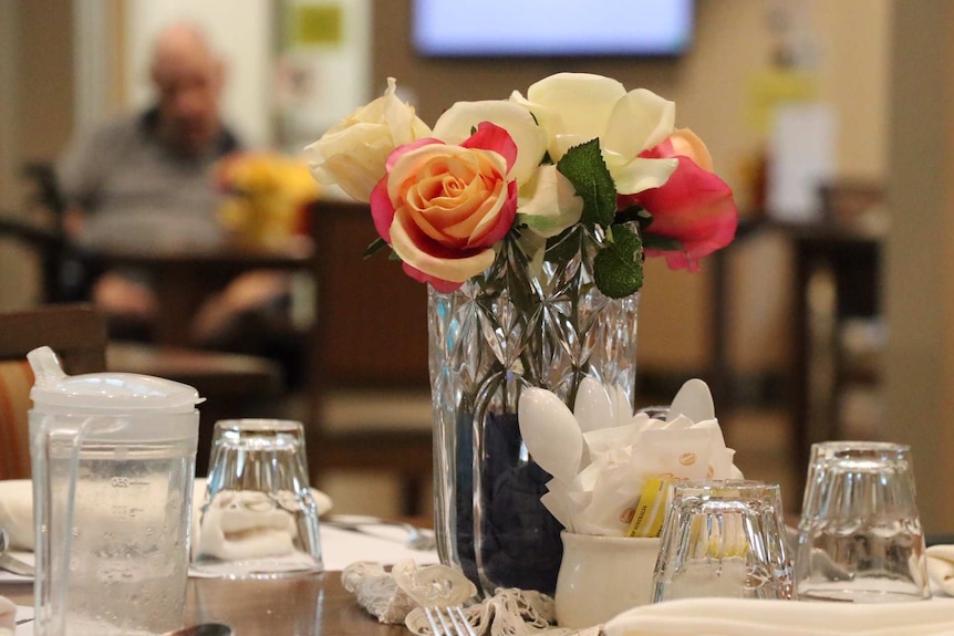 Dining table at a nursing home with an anonymous elderly man in the background.