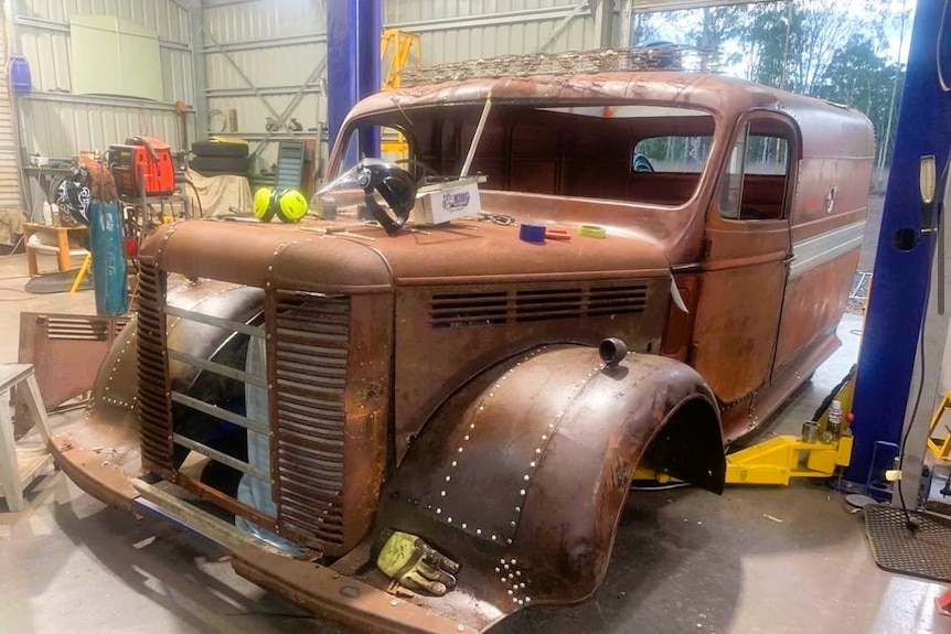 A rusty looking truck turned van in a backyard garage workshop.