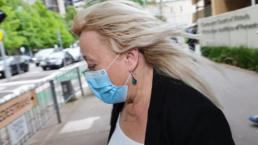 Woman's head and shoulders in profile, blonde hair blowing, wearing blue face mask.