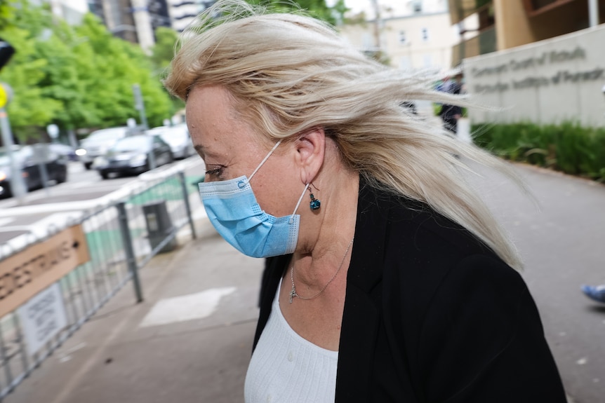 Woman's head and shoulders in profile, blonde hair blowing, wearing blue face mask.