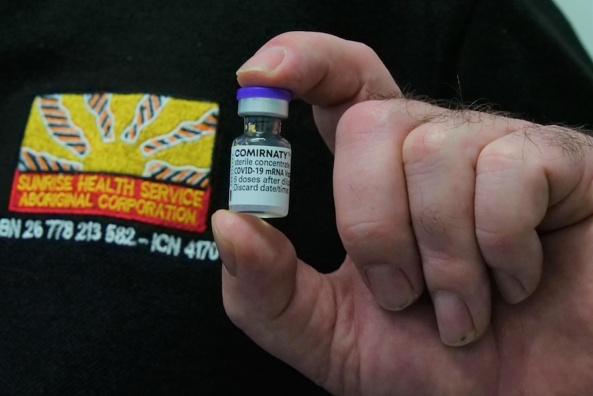 A man holds a vial of COVID vaccine showing the label