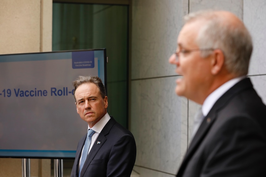 Greg Hunt looks across to Scott Morrison at a press conference