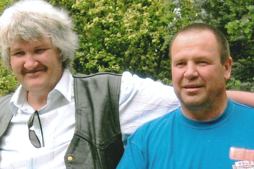 A photograph of two adult brothers. One man thick white hair puts his arm around his brother