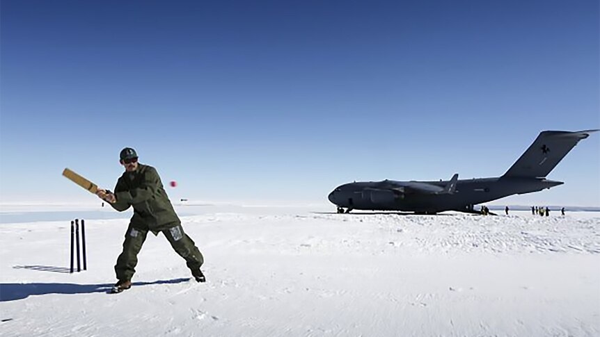 A man plays cricket on the ice in Antarctica in front of a military plane
